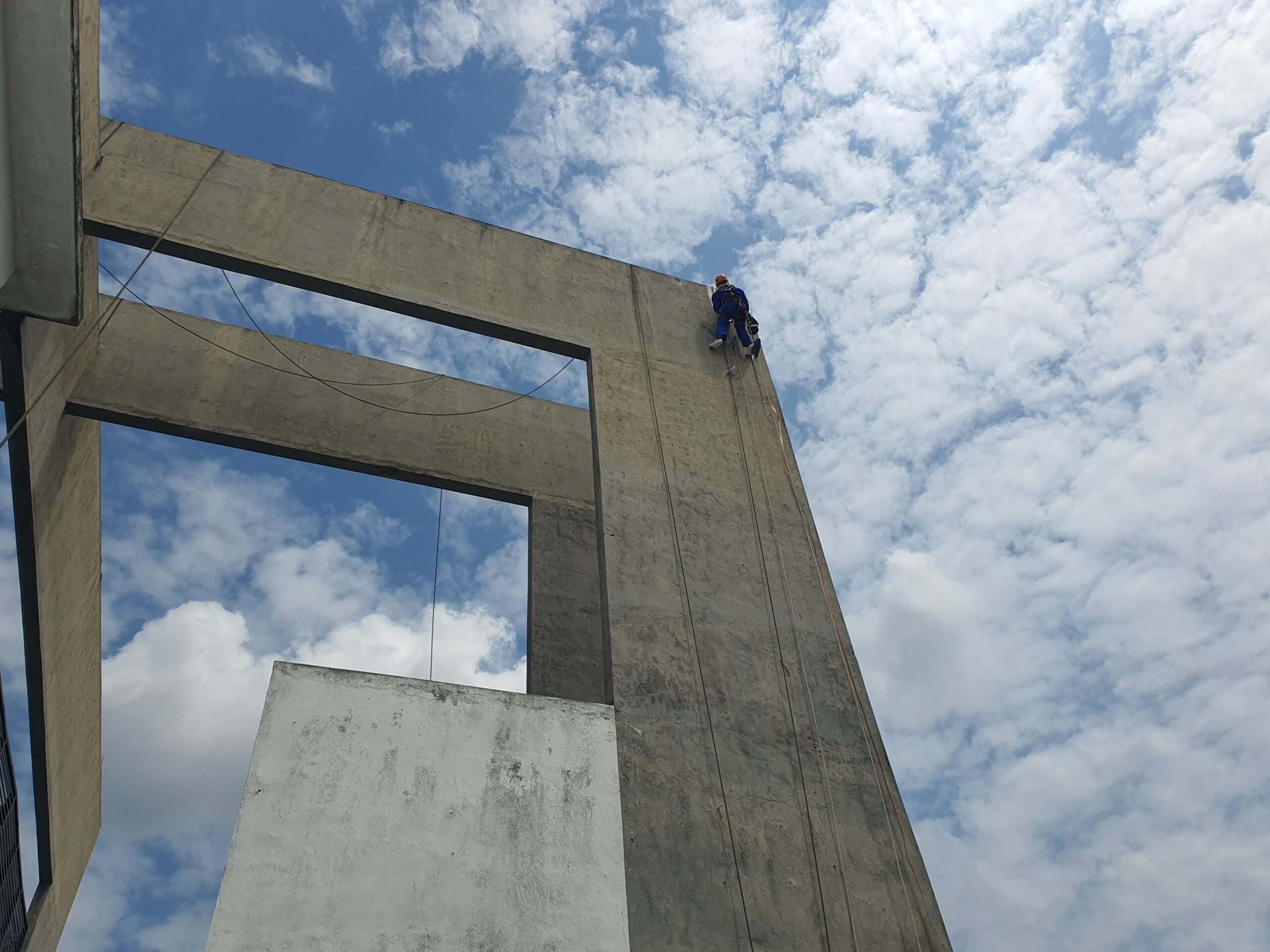 A Rope Access Safety Technician at protruding building facade, scaling upwards.