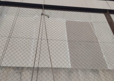 Wide view of a precast wall with chain-link safety netting and replaced cement board panels visible against the older surface