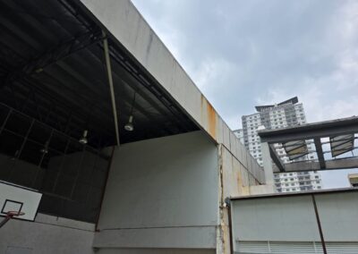 Rust staining running down cement board wall panels above a covered sports court at an international school in Kota Damansara, before repair