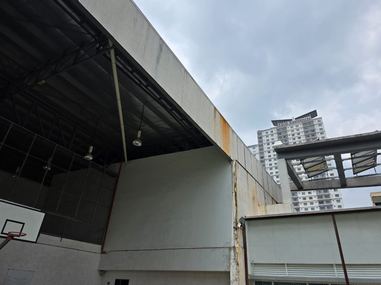 Rust staining running down cement board wall panels above a covered sports court at an international school in Kota Damansara, before repair