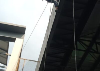 Wide low-angle view of two rope access technicians working near the roof edge of a school building