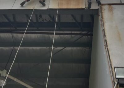 Two rope access technicians at a roof parapet treating a visibly rust-stained cement board panel