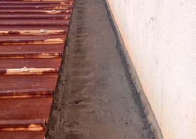Concrete gutter channel with fresh black waterproofing coating applied along the base and wall joint