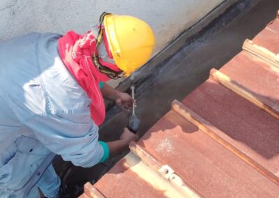 Close-up of a worker applying sealant to the joint between a concrete parapet wall and metal roof edge
