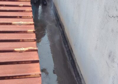 Two workers pressure-washing a concrete roof gutter channel as part of surface preparation before waterproofing