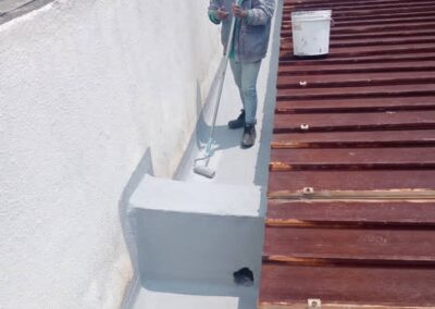 Worker using a long-handled roller to apply finishing coat inside a concrete gutter channel
