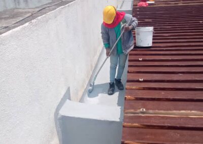 Technician applying waterproof coating by roller to a concrete box gutter upstand on a metal roof