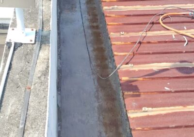 Technician inspecting a concrete box gutter on a metal roof before waterproofing works