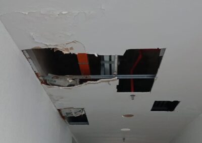 Close-up of a ceiling access hole cut into plasterboard, exposing the concrete slab and furring channels above for leak diagnosis
