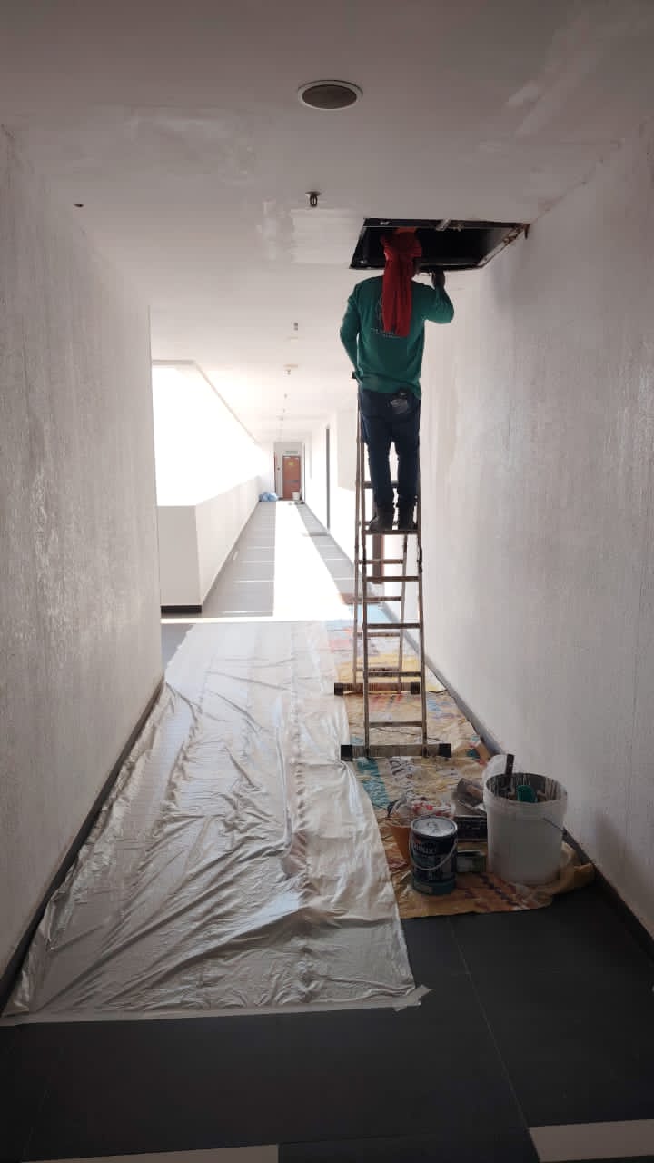 Technician accessing a condominium corridor ceiling cavity from a ladder to locate a concrete slab crack for PU injection repair