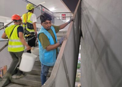 Three technicians working on an interior metal staircase, one wiping down a freshly painted handrail