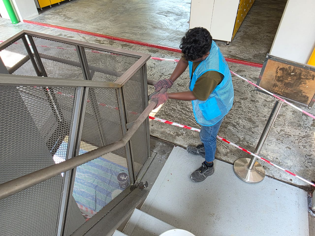 Technician sanding rust off a metal staircase handrail down to bare metal before repainting